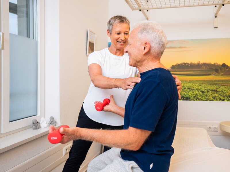 Therapeutin übt mit einem Patienten mit Hanteln