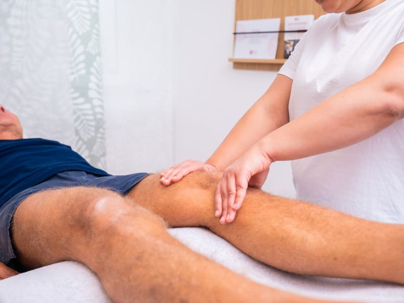 Therapeutin behandelt das Knie eines Patienten mit den Händen