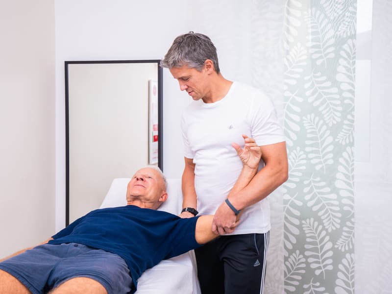 Therapeut bewegt den Arm eines liegenden Patienten